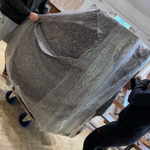 Large granite slab on a dolly wrapped in plastic, being moved by two people.",
