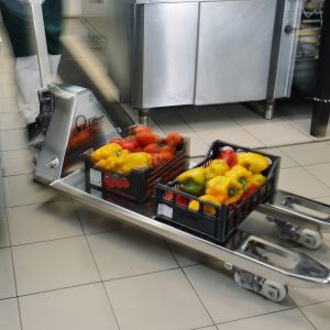 Crates of red and yellow bell peppers on a metal cart in a commercial kitchen.